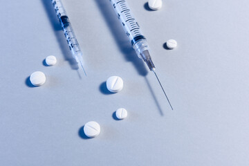 Two syringes entering the frame, surrounded by a few pills, on blue background