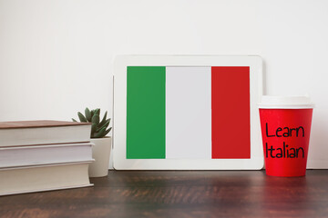 National flag of Italia on the tablet, textbooks, a red cup of hot drink coffee or tea on the...