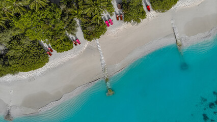 Fototapeta na wymiar Luftaufnahme eines Strand mit Palmen, Sonnenliegen, Sonnenschirmen und kristallklarem türkis blauen Wasser mit seichten Wellen auf einer traumhaften Insel auf den Malediven