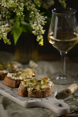 Bruschetta with gorgonzola cheese and pears, nuts on wooden table with textile, glass of white wine and beautiful flowers. Selective focus, copy space. 