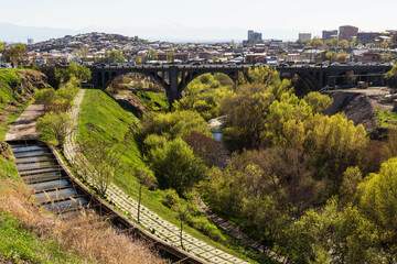 Yerevan, Armenia - April 2022: The park with a river, a bridge with cars and the mountain of Ararat in the background with a snow peak and the view over the city