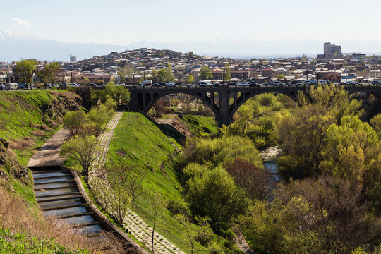 Yerevan, Armenia - April 2022: The park with a river, a bridge with cars and the mountain of Ararat in the background with a snow peak and the view over the city