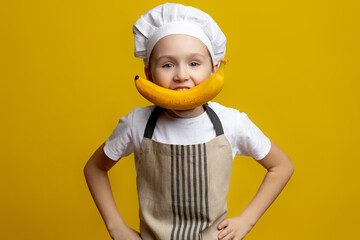 Happy little chef boy with yellow banana smile on isolated yellow background