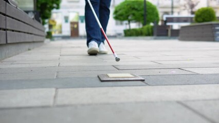 Young blind man with with a cane alone outdoors. Male person wearing glasses and casual clothes. Independence concept