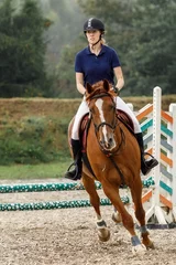 Foto op Canvas Young horse rider girl on show jumping course in equestrian sports competition. Vertical photo © Linas T
