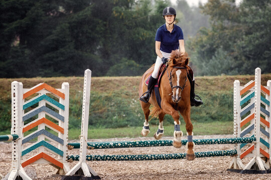 A young female rider completing a jump.