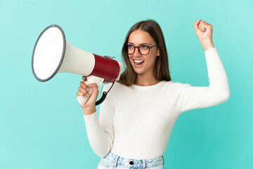 Young woman over isolated blue background shouting through a megaphone to announce something in...