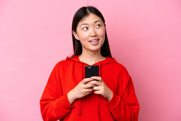 Young Chinese woman isolated on pink background using mobile phone and looking up