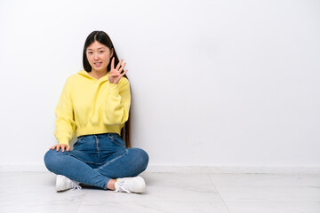 Young Chinese woman sitting on the floor isolated on white wall happy and counting four with fingers