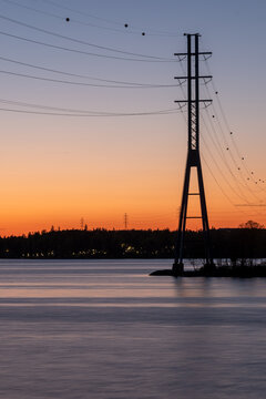 Silhouette of a tall electricity pylon against a vivid sunset. Power lines crossing the night sky.
