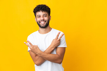 Young Moroccan man isolated on yellow background smiling and showing victory sign