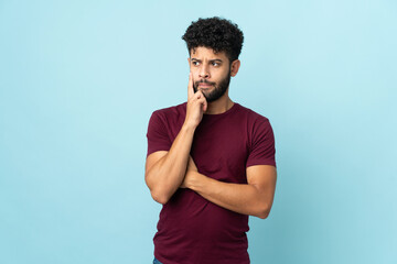 Young Moroccan man isolated on blue background having doubts and thinking