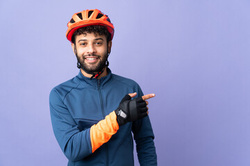Young Moroccan cyclist man isolated on purple background pointing finger to the side - obrazy, fototapety, plakaty