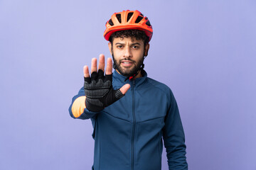Young Moroccan cyclist man isolated on purple background making stop gesture - obrazy, fototapety, plakaty