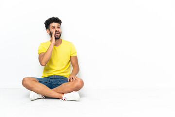 Fototapeta premium Young Moroccan handsome man sitting on the floor over isolated background shouting with mouth wide open to the lateral
