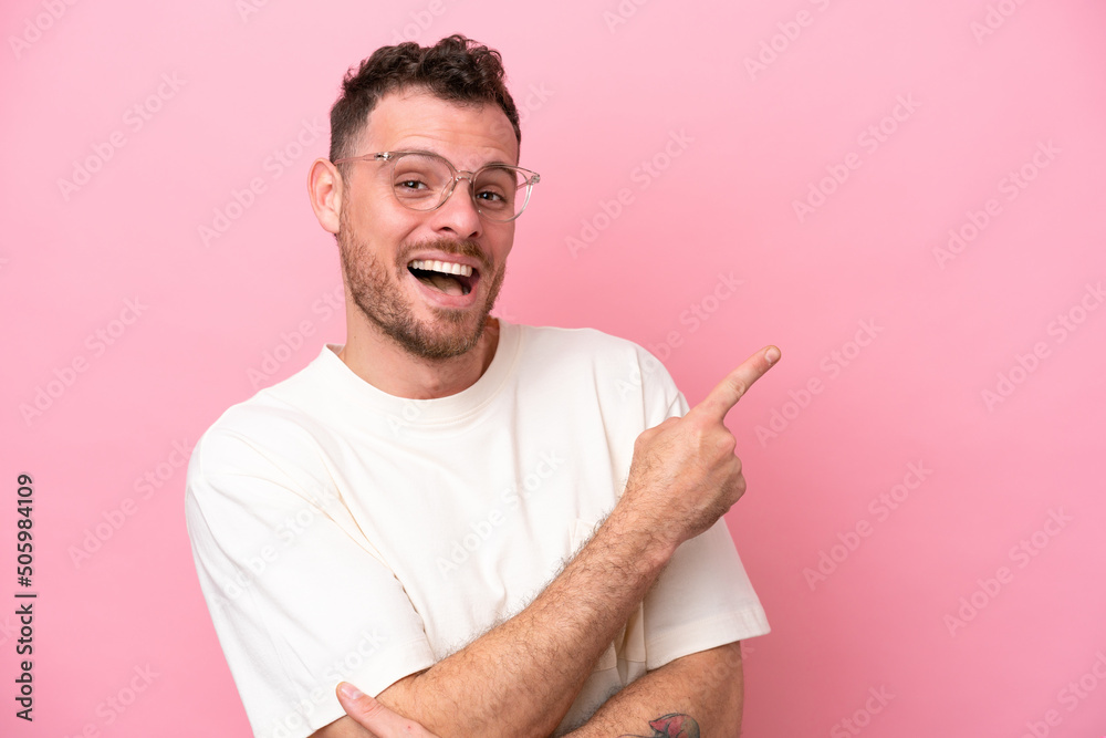 Wall mural Young brazilian man isolated on pink background With glasses and pointing side