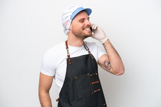 Fishmonger man wearing an apron isolated on white background keeping a conversation with the mobile phone