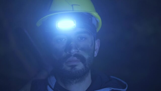 Tired miner looking at camera.
Mandeci looks around with the light of a lantern in the dark. He has black dirt on his face.

