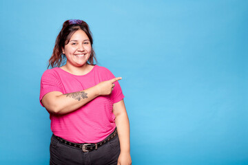 Young curvy latina woman smiling and showing copy blank space isolated over blue background