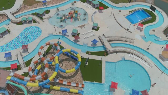 aerial footage of several long winding pools with colorful waterslides and colorful umbrellas around the pool near a lake surrounded with lush green grass at Lake Spivey Recreation Center in Jonesboro