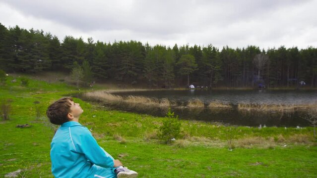 Deep breathing boy by the lake.
The child sitting by the lake takes a deep breath and exhales against the forest and lake view. Peaceful and serene.
