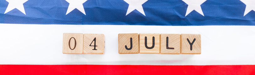 Date of 4th july on the wooden cubes and american flag on the wooden background.