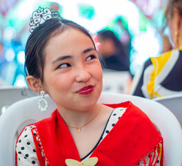Beautiful asian little girl with traditional dress in a stand at the Seville Fair in Spain looks smiling