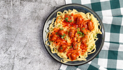 Tagliatelle pasta with sausages and tomato sauce on a round plate on a dark gray background. Top view, flat lay