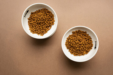 two bowls with dry pet food on a brown background.