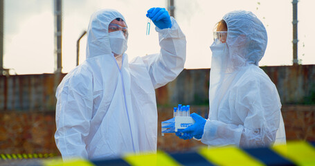 Scientist in protective suit, mask and gloves collect sample of waste water and toxic water from factory  took a sample of waste water for analysis