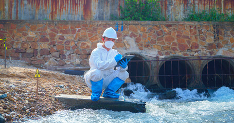 Asian man scientist researcher in protective suit takes water for analysis of contaminated water sources. Wastewater and environmental problems. Environment Issue concept