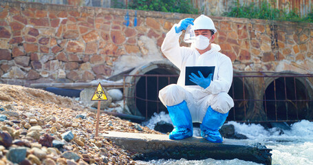 Asian man scientist researcher in protective suit takes water for analysis of contaminated water sources. Wastewater and environmental problems. Environment Issue concept