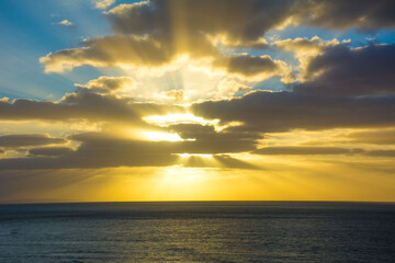 Sun rays bursting through the clouds during a sunrise over the Pacific ocean