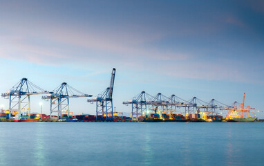 Fototapeta na wymiar Container cargo ship with crane bridge working in shipyard at dusk.