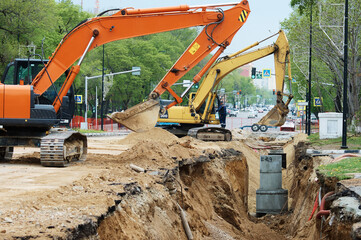 Reconstruction of the underground sewerage system on a city street in spring. Two excavators are...