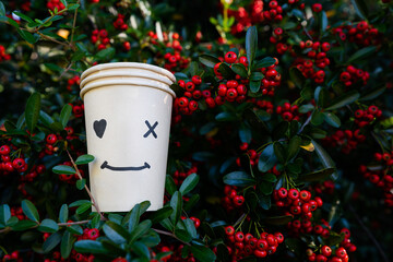Disposable paper eco-cups against  green lush foliage plants and red seeds background.