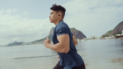 Fototapeta na wymiar Young man running while listening to music on his headphones at the Rio de Janeiro beach.