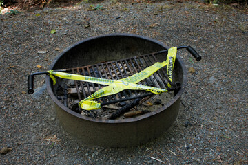A view of yellow caution tape covering a campground fire pit during a provisional fire use ban.