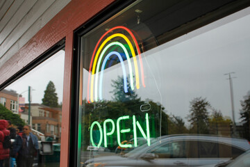 A view of a neon open sign, featuring a rainbow symbol.