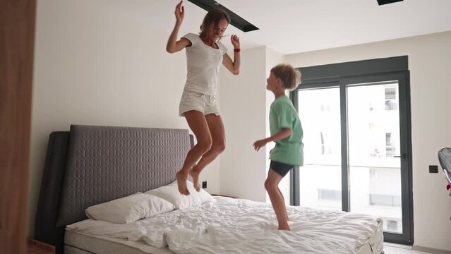 Happy mom have fun jumping with little son on bed. Slow motion