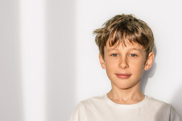 Portrait of a white caucasian 9 year old boy in a white t-shirt. The child looks directly into the camera with a slight smile. copy space left