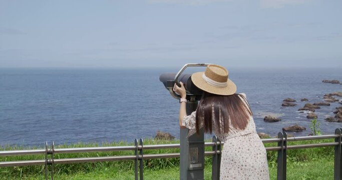Tourist woman look at tourist binocular to see the ocean