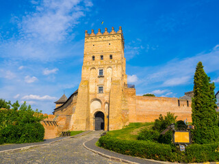 Fototapeta na wymiar Lutsk High Castle, also known as Lubart's Castle. Ukraine. Brick Tower and Walls. A part of defence wall of Lutsk Castle. The Entrance tower against the blue sky and with greenery under a brick wall.