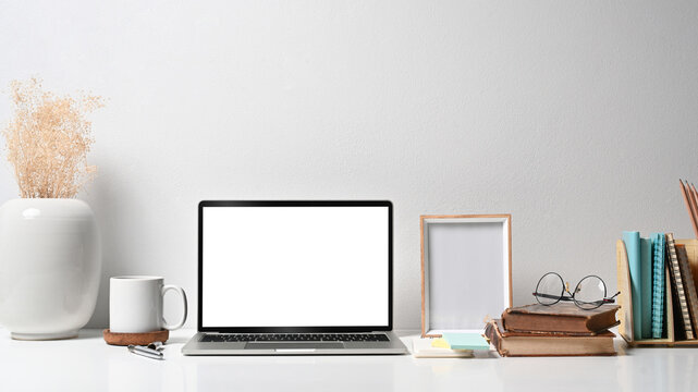 Comfortable workplace with laptop computer, picture frame, flower pot, coffee cup and stationery on white table