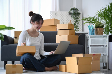 Young business woman answering customers through laptops and preparing parcel boxes of product for...