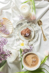Top view of breakfast in bed with antique tableware, cup of coffee and chocolate profiterole, decor of spring flowers.