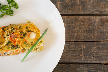 A piece of Pie made from fish, eggs, onions and carrots. White plate, wooden planks