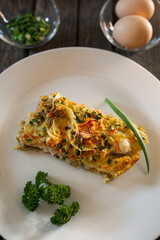 A piece of Pie made from fish, eggs, onions and carrots. White plate, wooden planks