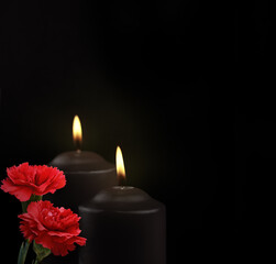 Obraz na płótnie Canvas Two black burning candles and of carnation flowers on dark background