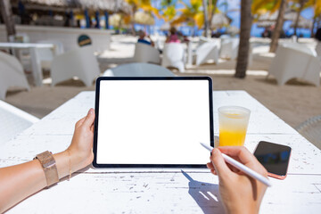 Woman using tablet with stylus pen in tropical beach bar, blank white screen mockup